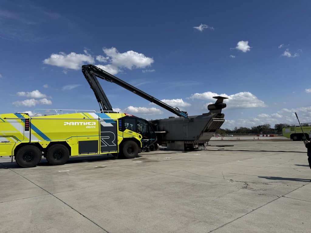 ARFF crash truck with high-reach extendable turret beside an aircraft fire trainer
