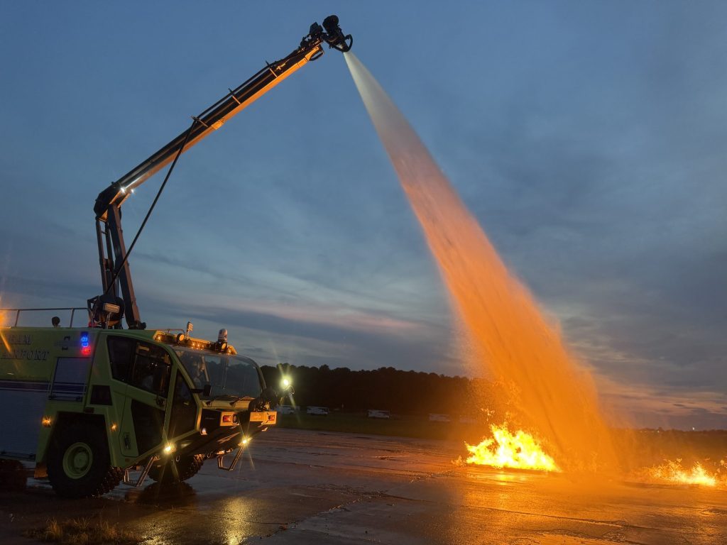 ARFF truck boom flowing agent onto a fire at dusk