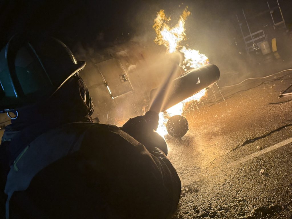 Firefighter directing a hose stream at a burning engine prop at night