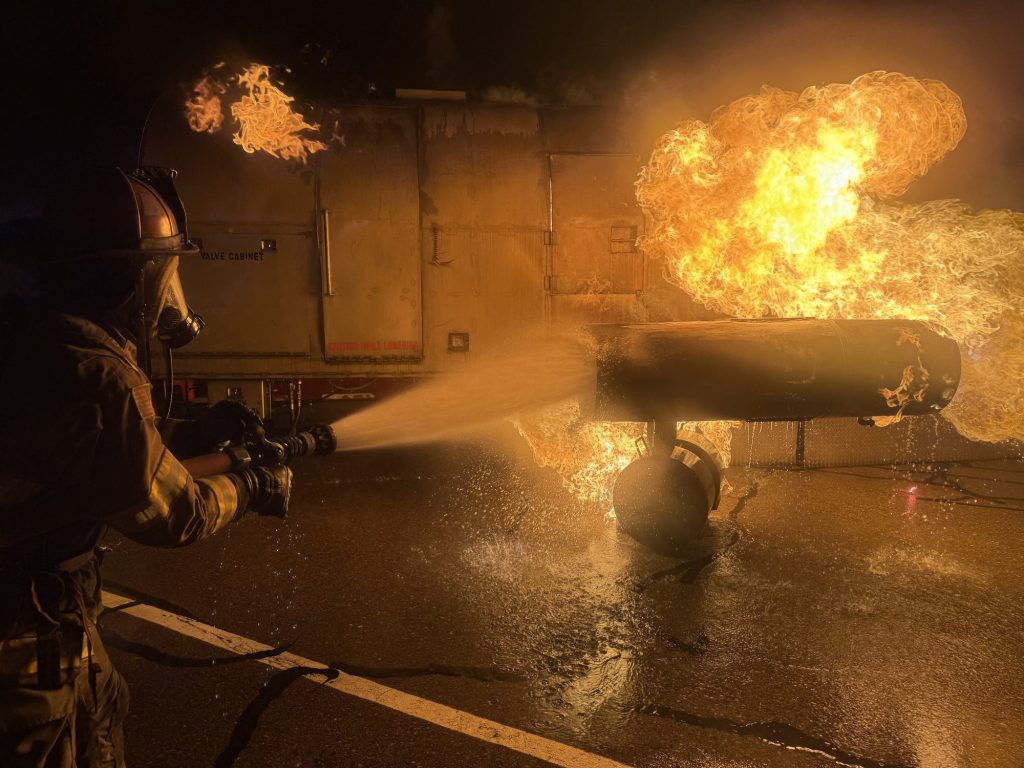 Firefighter flowing a hose stream onto an aircraft engine fire at night