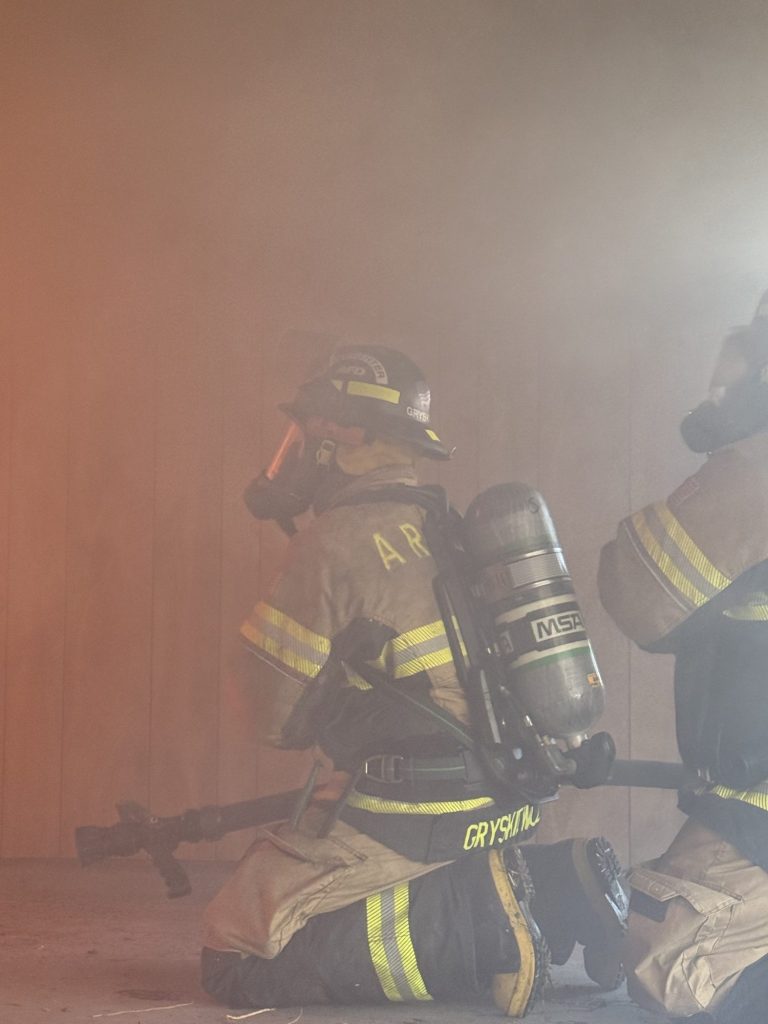 Firefighters on air advancing a hose line on their knees in heavy smoke