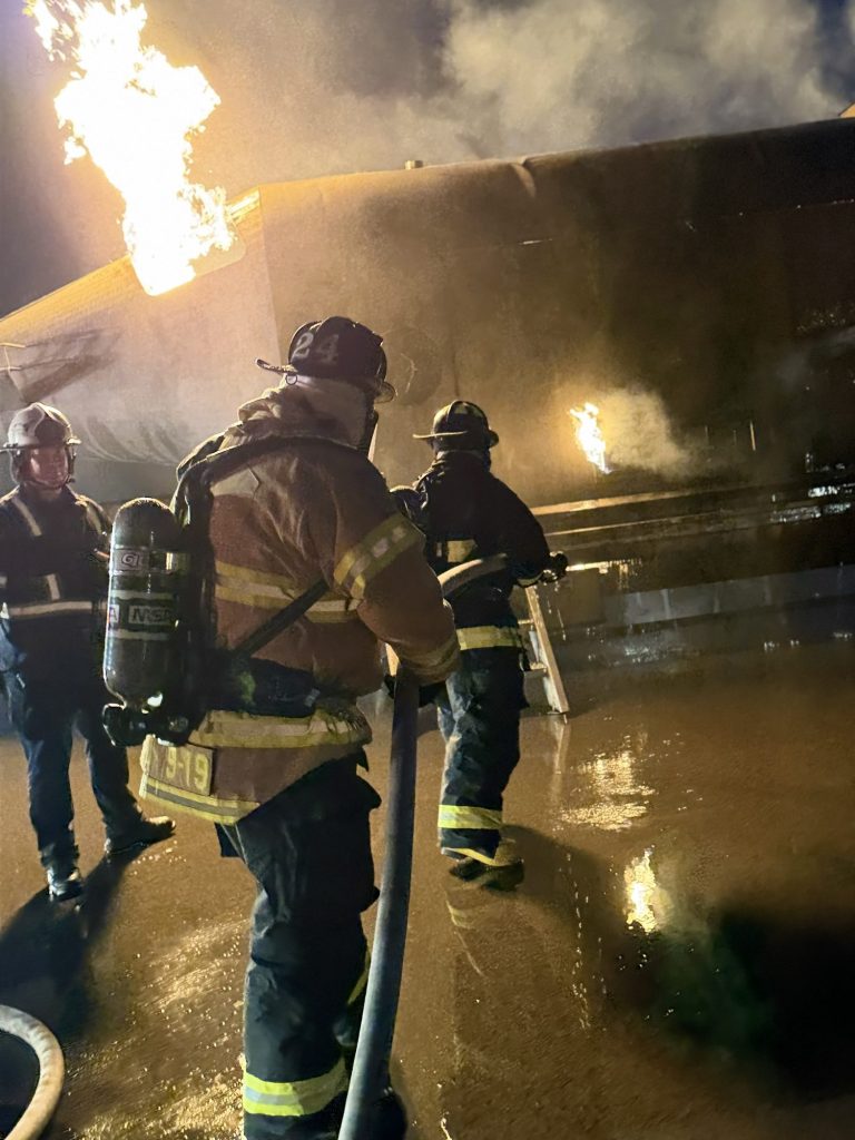 Firefighters advancing a hose line on an aircraft fire at night