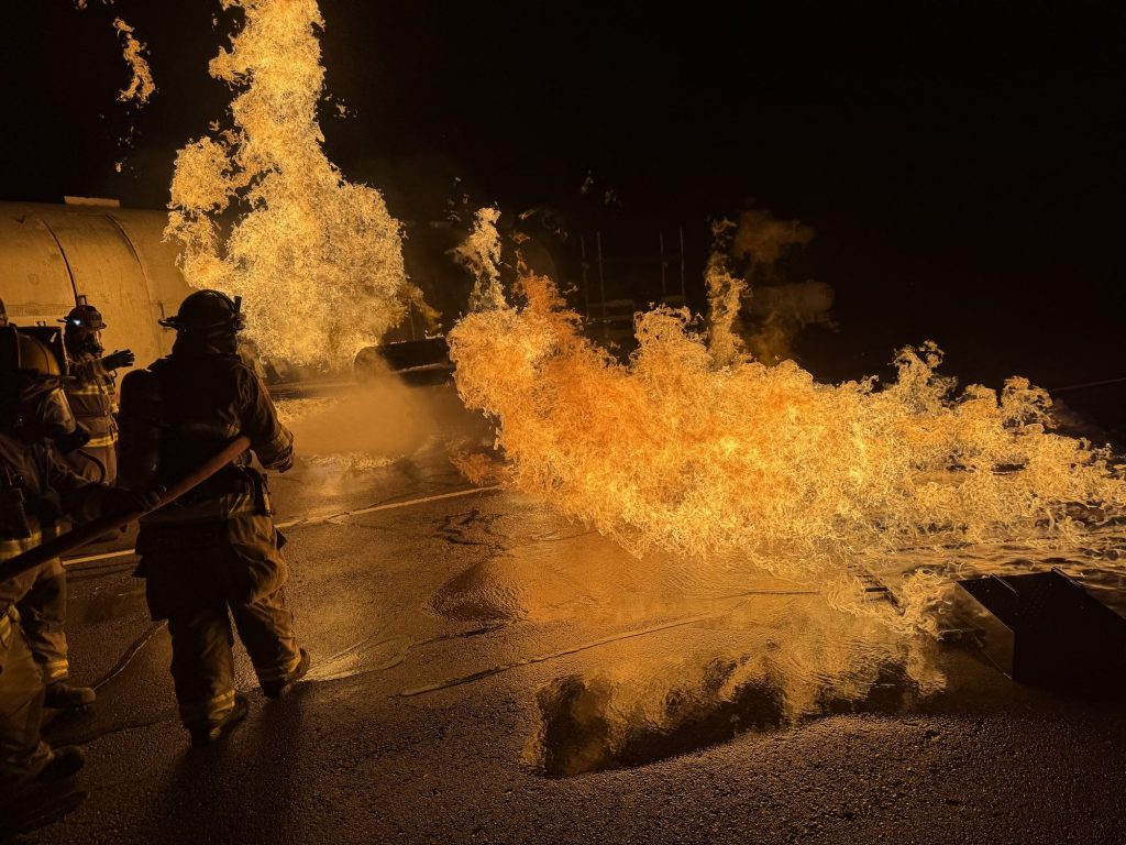 Hose team pushing back a running fuel spill fire at night