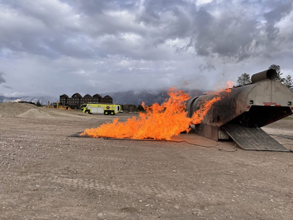 Fuel fire burning beside an aircraft trainer with ARFF trucks behind