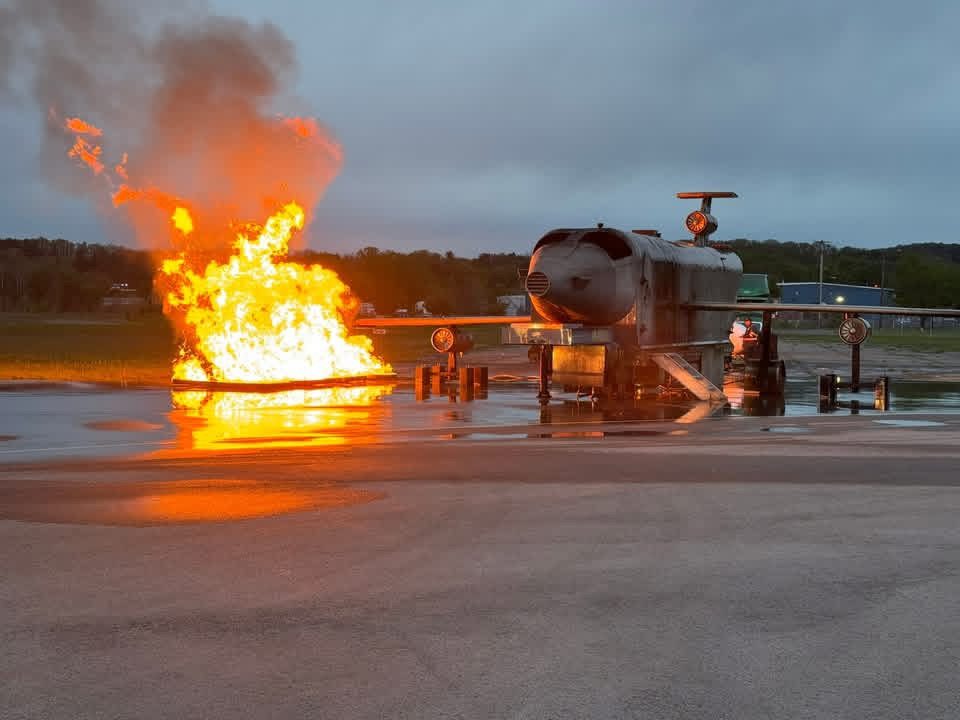 Fuel pan fire burning beside a mobile aircraft fire trainer at dusk