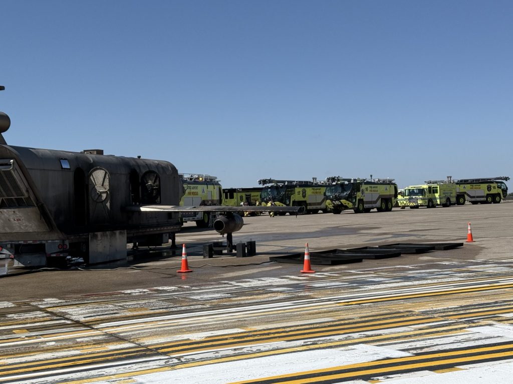 Line of ARFF crash trucks staged on the ramp behind a mobile aircraft fire trainer and fuel pans