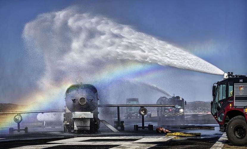 ARFF truck turret flowing water over the aircraft fire trainer and forming a rainbow