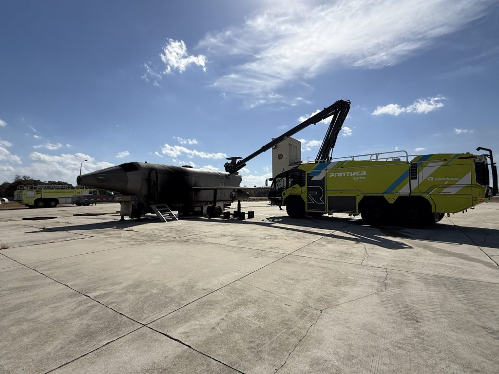 Electric ARFF truck with its high-reach extendable turret positioned over the aircraft fire trainer