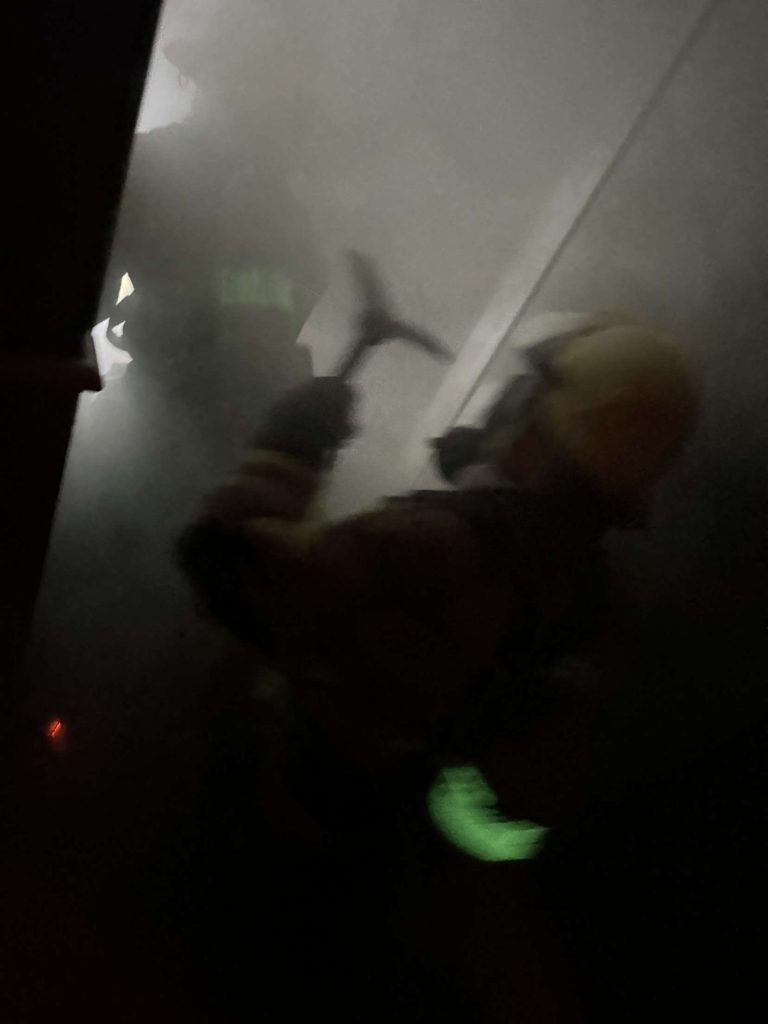 Firefighter with a hand tool in dark smoke during a search drill