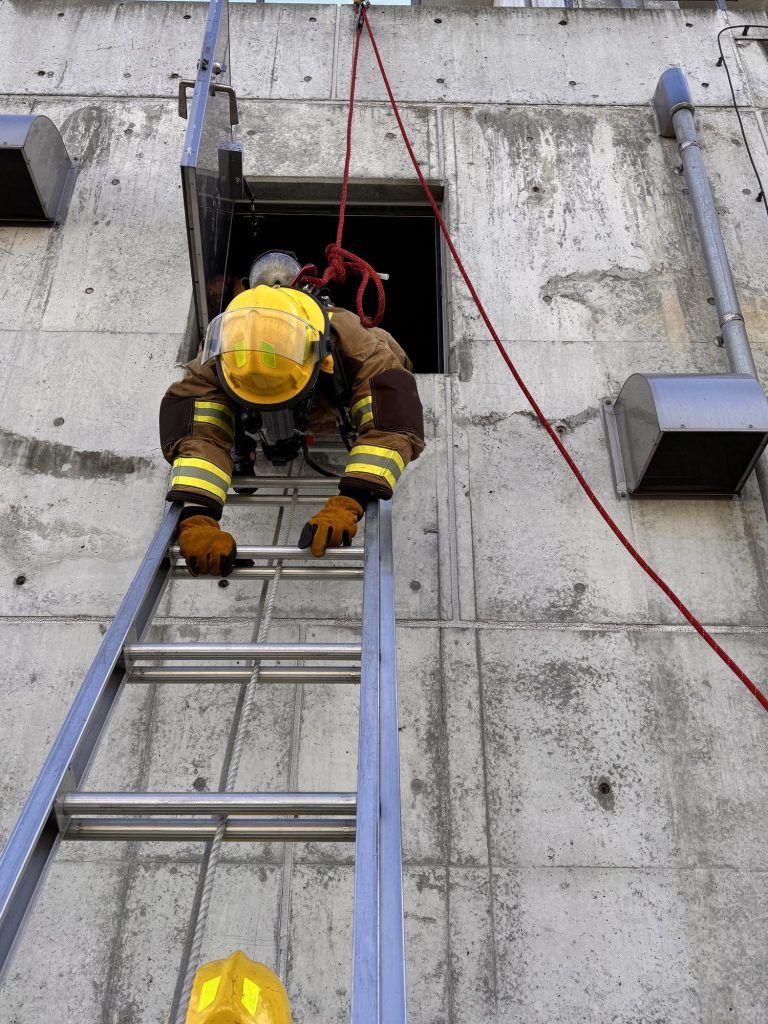 Firefighter climbing out a tower window onto a ladder during a bailout drill