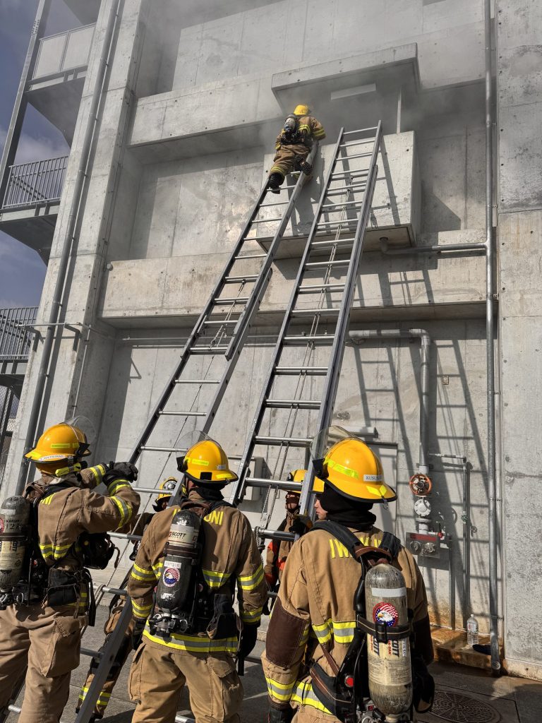 Firefighters raising ground ladders to a concrete training tower