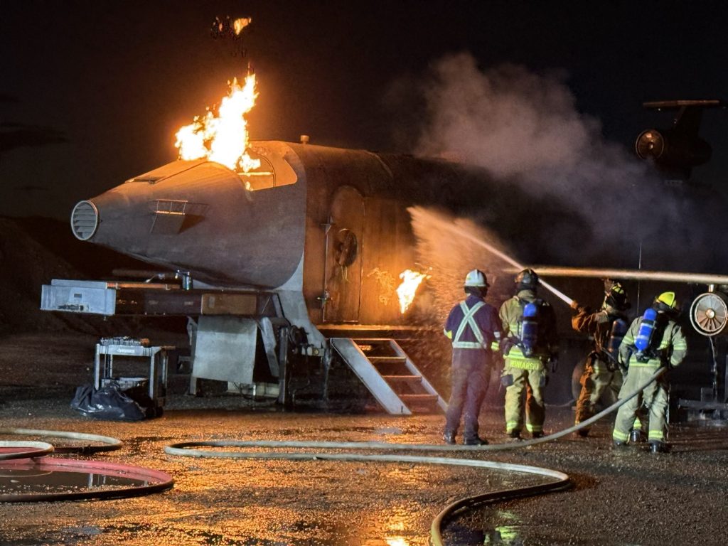 Hose team with an instructor attacking a nose and fuselage fire on the aircraft trainer at night