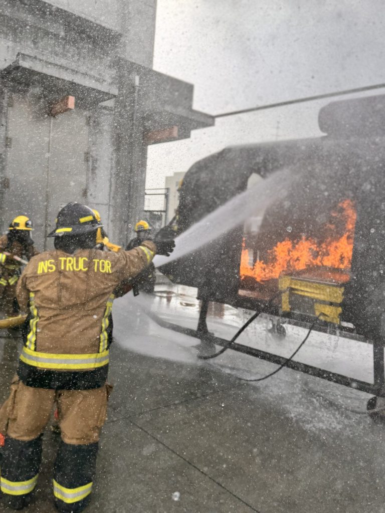 Instructor flowing a hose stream on a burning aircraft trainer