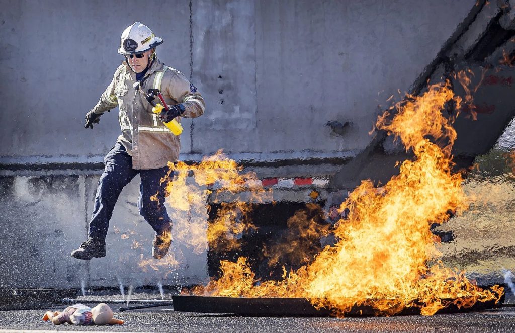 Instructor leaping over a burning fuel pan beside the aircraft fire trainer