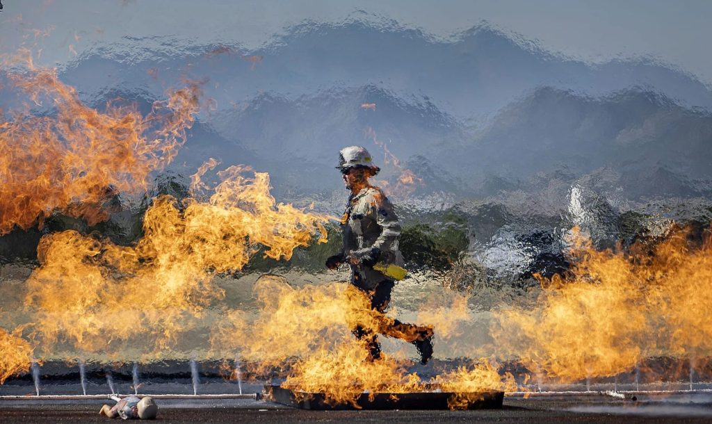 Instructor running past fuel pan fires behind a curtain of water spray