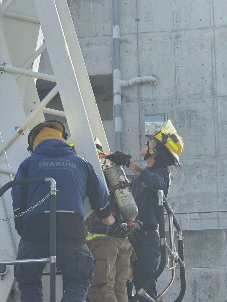 Instructor helping a firefighter on a training tower ladder