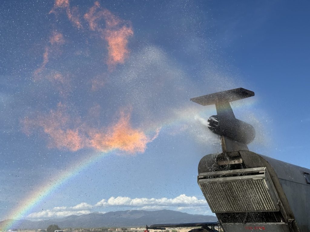 Water spray and a rainbow over the tail engine of the aircraft fire trainer with mountains behind