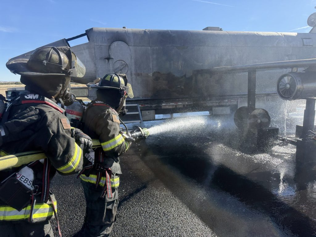 Two firefighters in full PPE and SCBA flowing a handline at the aircraft trainer's wing engine